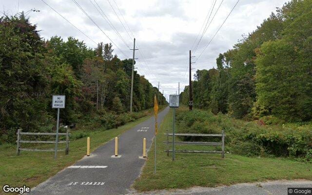 The Middle Township Bike Path at Reeves Street, a paved trail with yellow bollards and a No Motor Vehicles sign, running north under Atlantic City Electric power lines between rows of trees